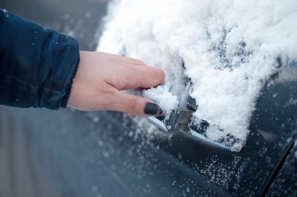 A hand about to open a car door that is covered in snow.